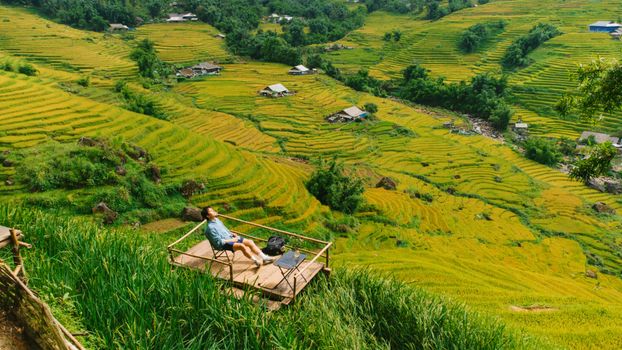 A person enjoys a tranquil moment on a deck with stunning views of vibrant rice terraces under sunlight.