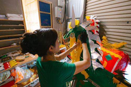 Free A woman intricately working on a colorful dragon decoration in a workshop. Stock Photo