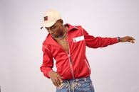 Young black male in stylish wear and necklace looking down while standing with reached arm