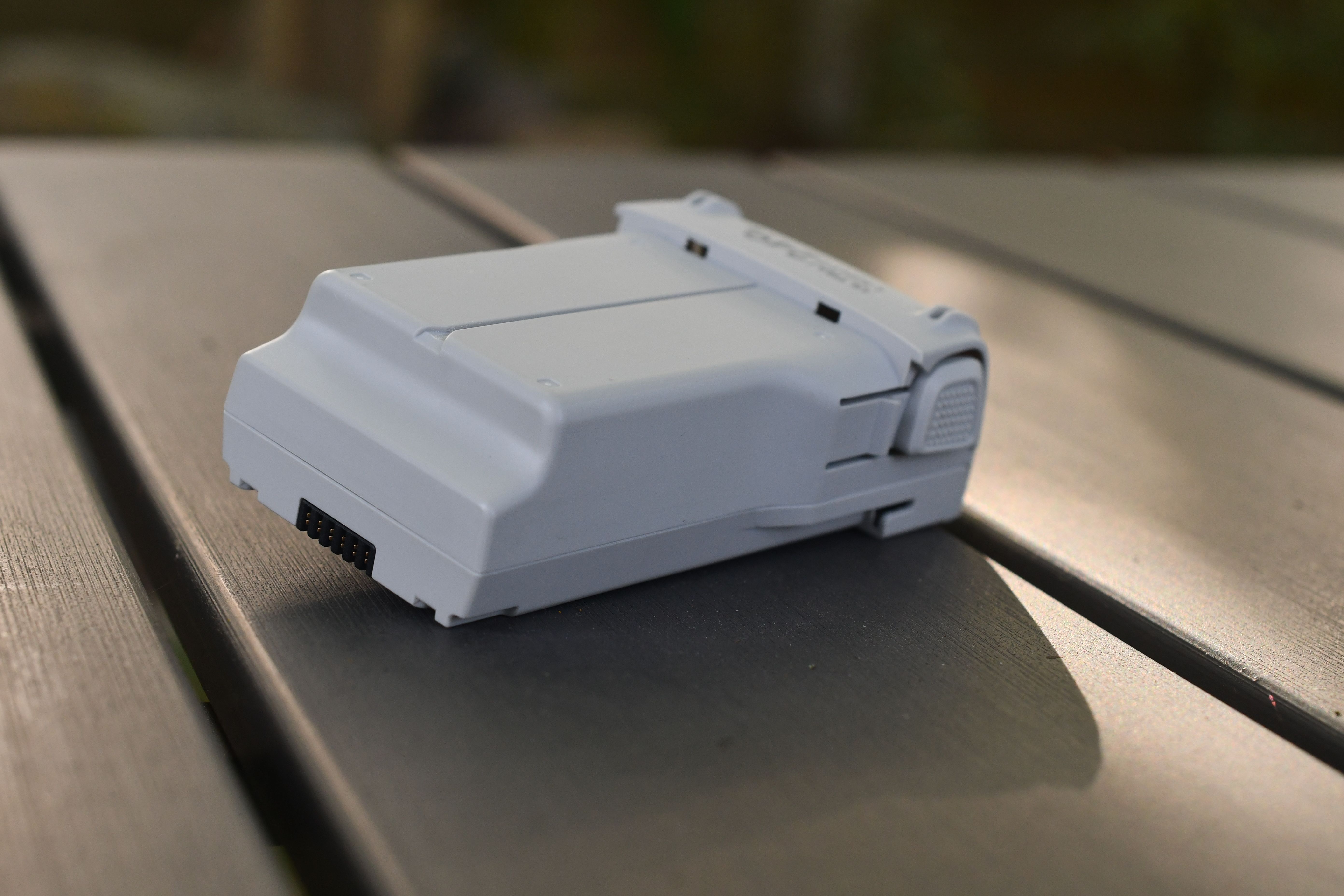 Close-up of a modern drone battery on a wooden table outdoors.