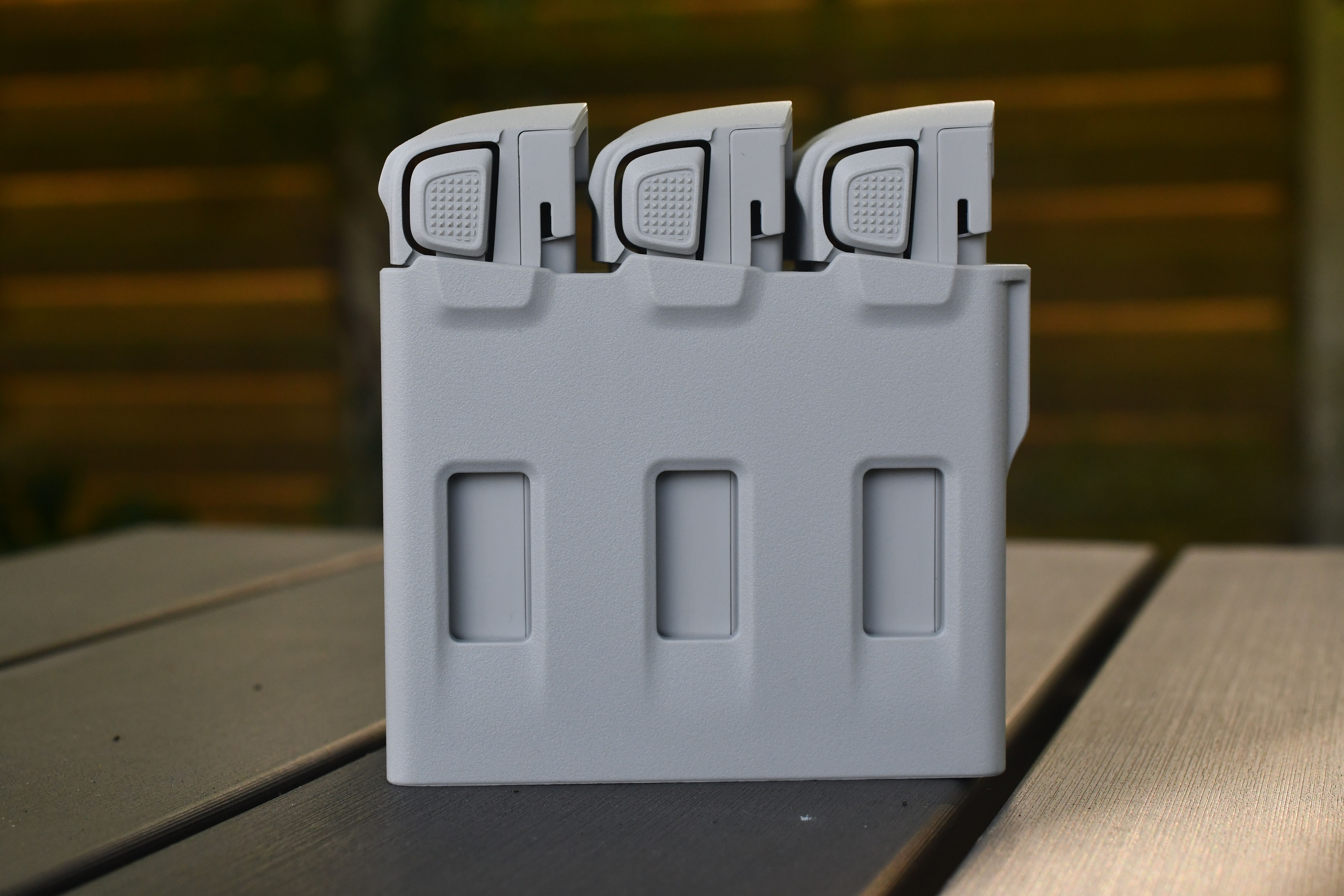 Gray battery storage case with three compartments on an outdoor wooden table