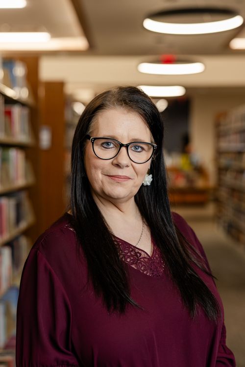 Free Professional woman in library with bookshelves, wearing glasses. Stock Photo