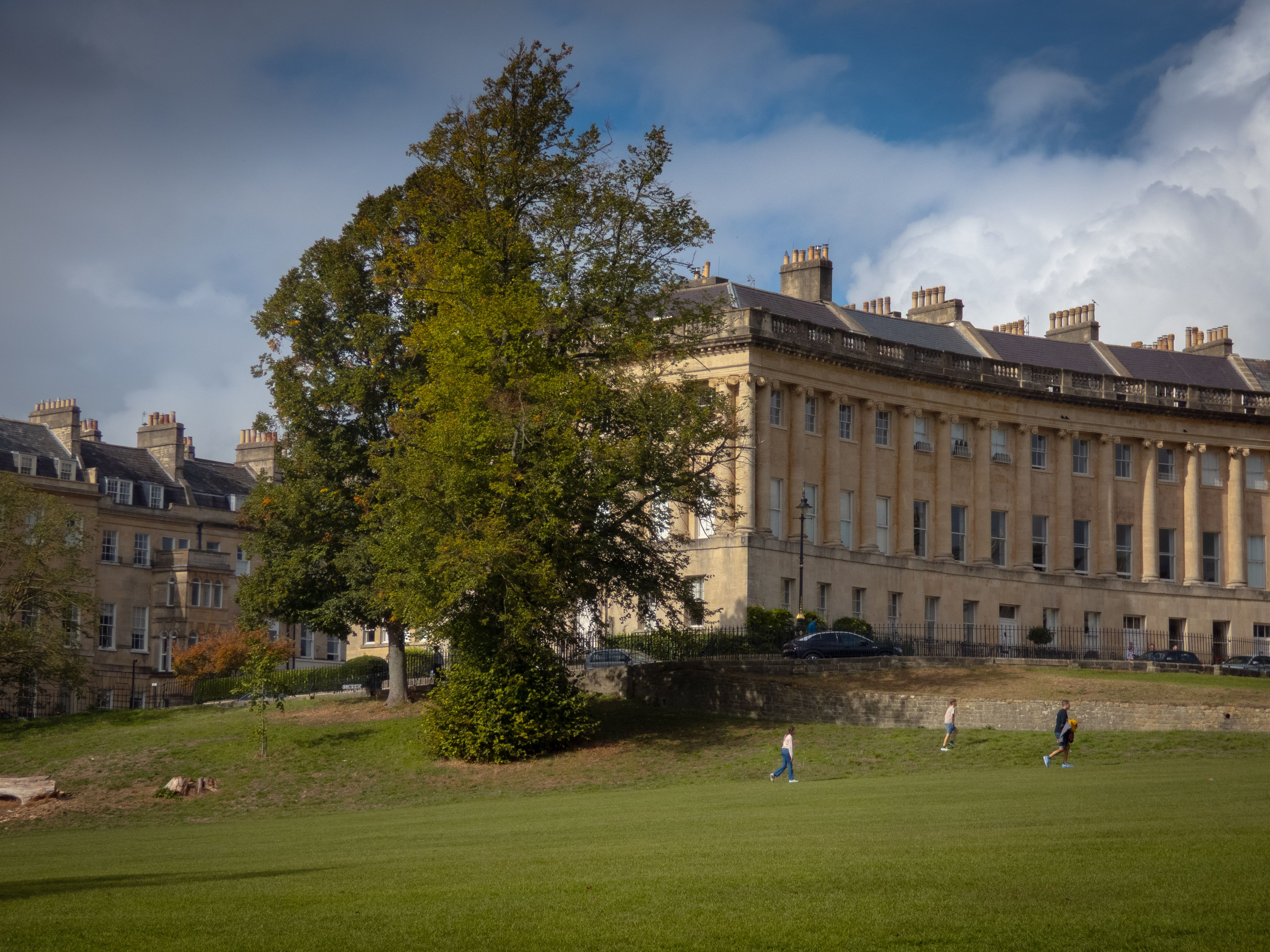 Scenic view of the historic Royal Crescent with lush greenery and cloudy sky.