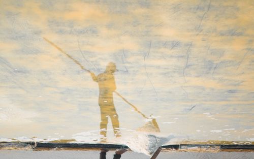 Free Abstract image of a fisherman with a pole reflected in tranquil water. Stock Photo