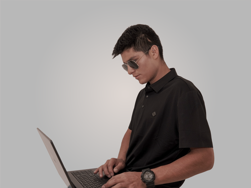 Free Stylish young man wearing sunglasses and a black polo, using a laptop against a neutral background. Stock Photo