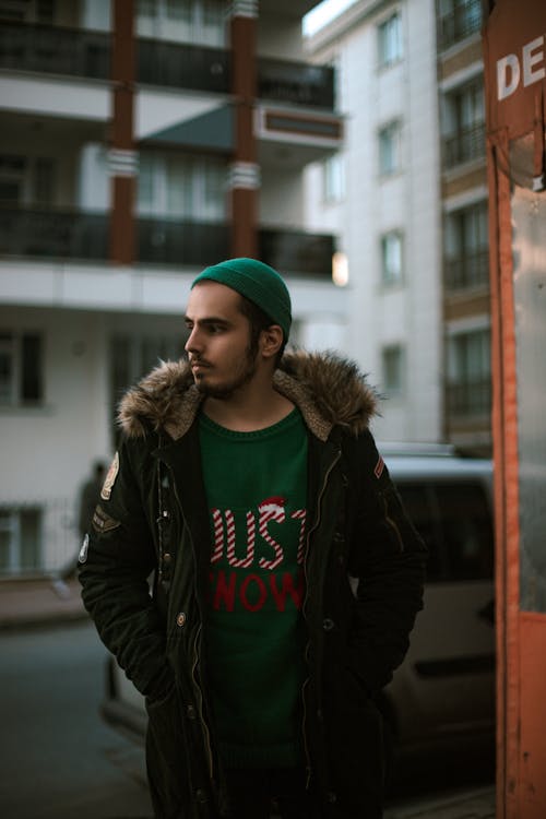 Man in Black Jacket and Green Knit Cap Standing Near Building