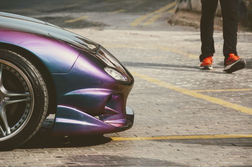 Free Close-up of a purple sports car next to a person in vivid sneakers on a cobblestone street. Stock Photo