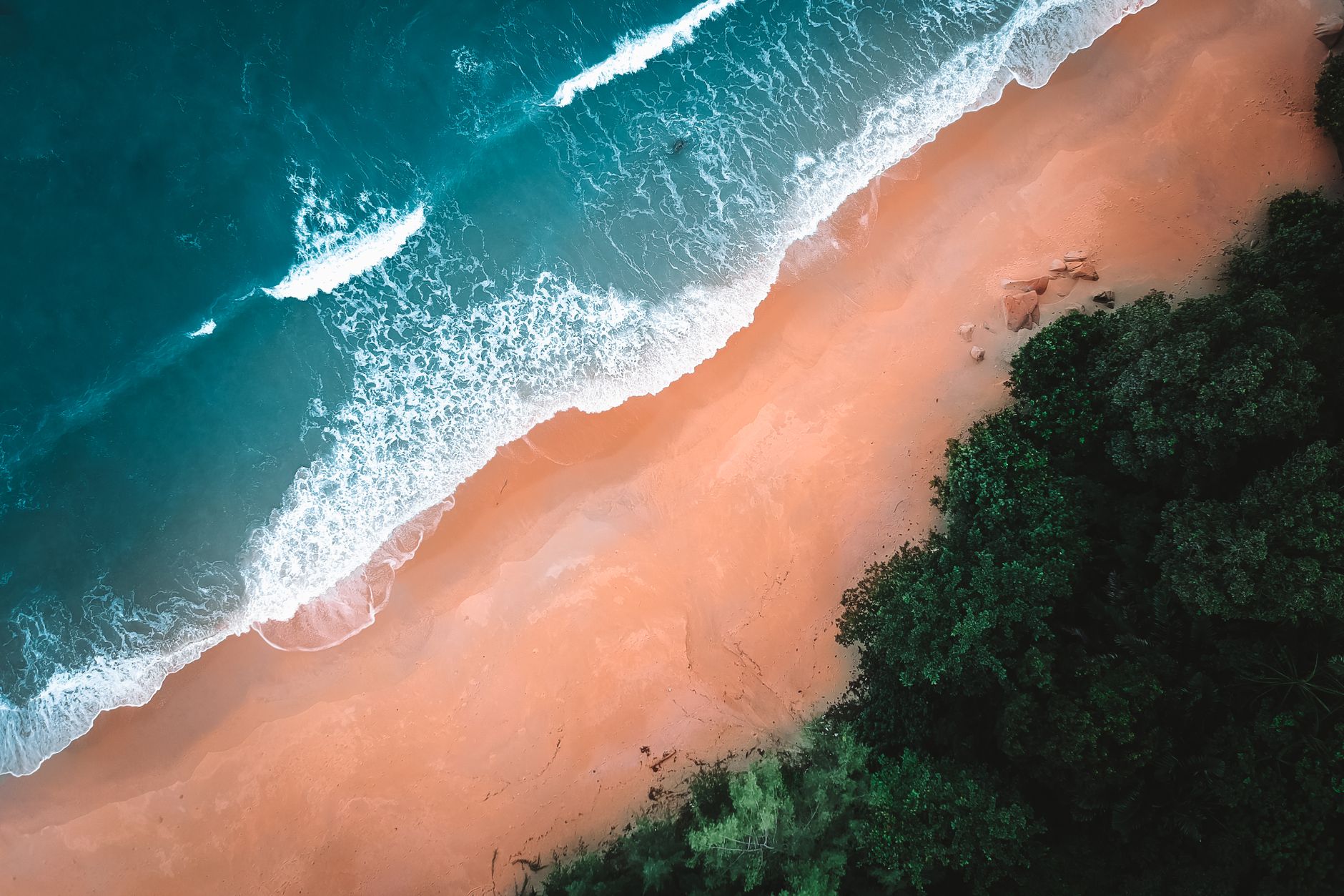 Breathtaking aerial view of waves crashing on a sandy beach, surrounded by lush greenery.