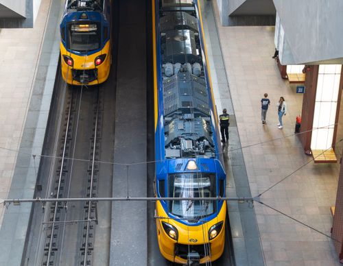Free Overhead view of two yellow-blue trains at an indoor city station with passengers. Stock Photo