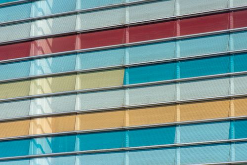 Free Close-up of a vibrant glass facade with red, blue, and yellow panels creating a modern architectural look. Stock Photo
