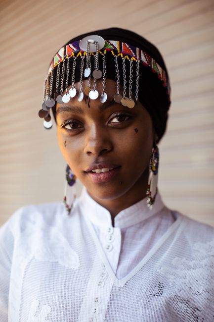 Captivating portrait of a woman wearing a colorful beaded headdress with dangly jewelry.