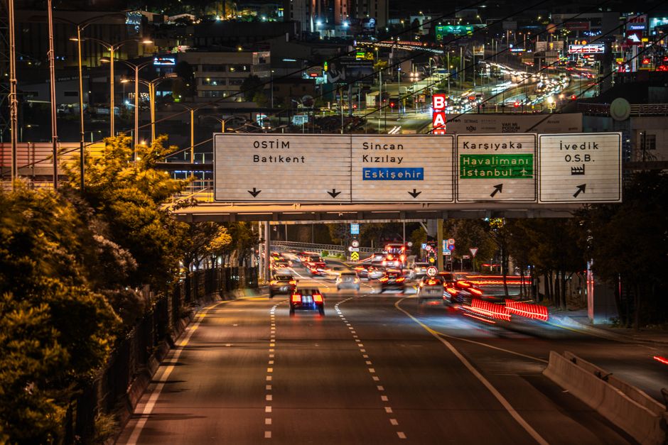 Vibrant night view of bustling traffic under illuminated road signs in Ankara, Türkiye.