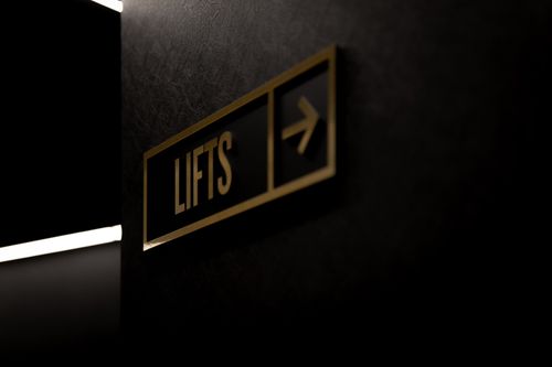 Free Sleek black and gold elevator sign pointing right against a dark background. Stock Photo