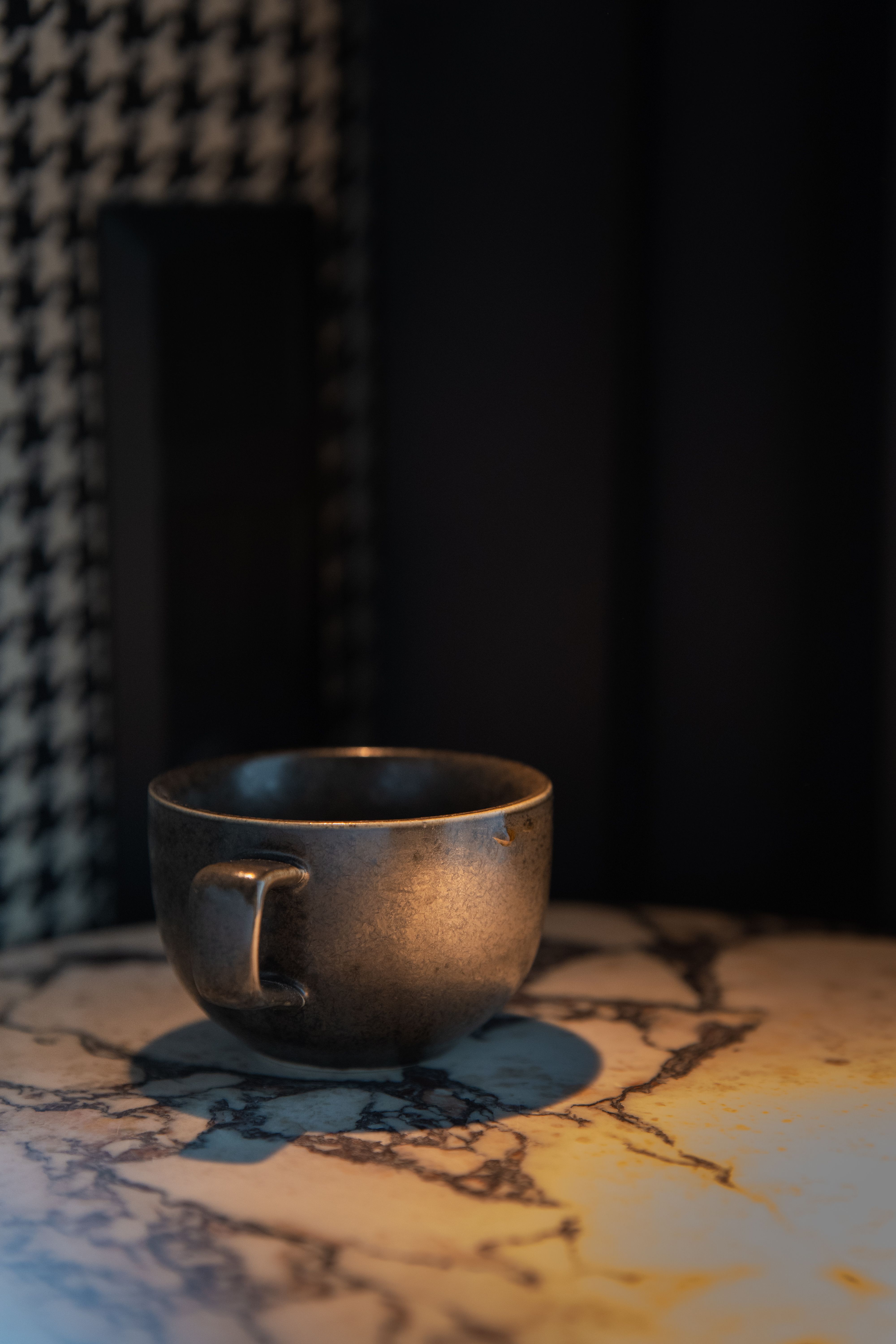 Fotomural Una taza de café rústica de cerámica sobre una superficie de mármol con sombras y patrones texturizados.