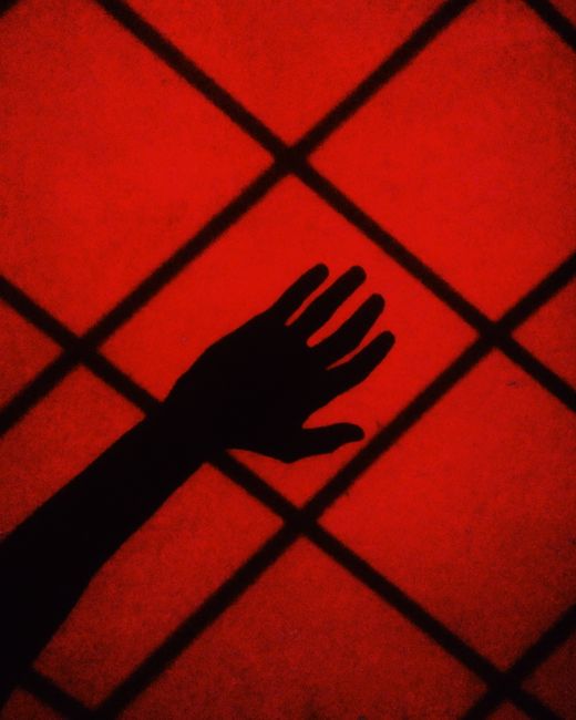 Silhouette of a hand against a vibrant red geometric background with a pattern of squares.