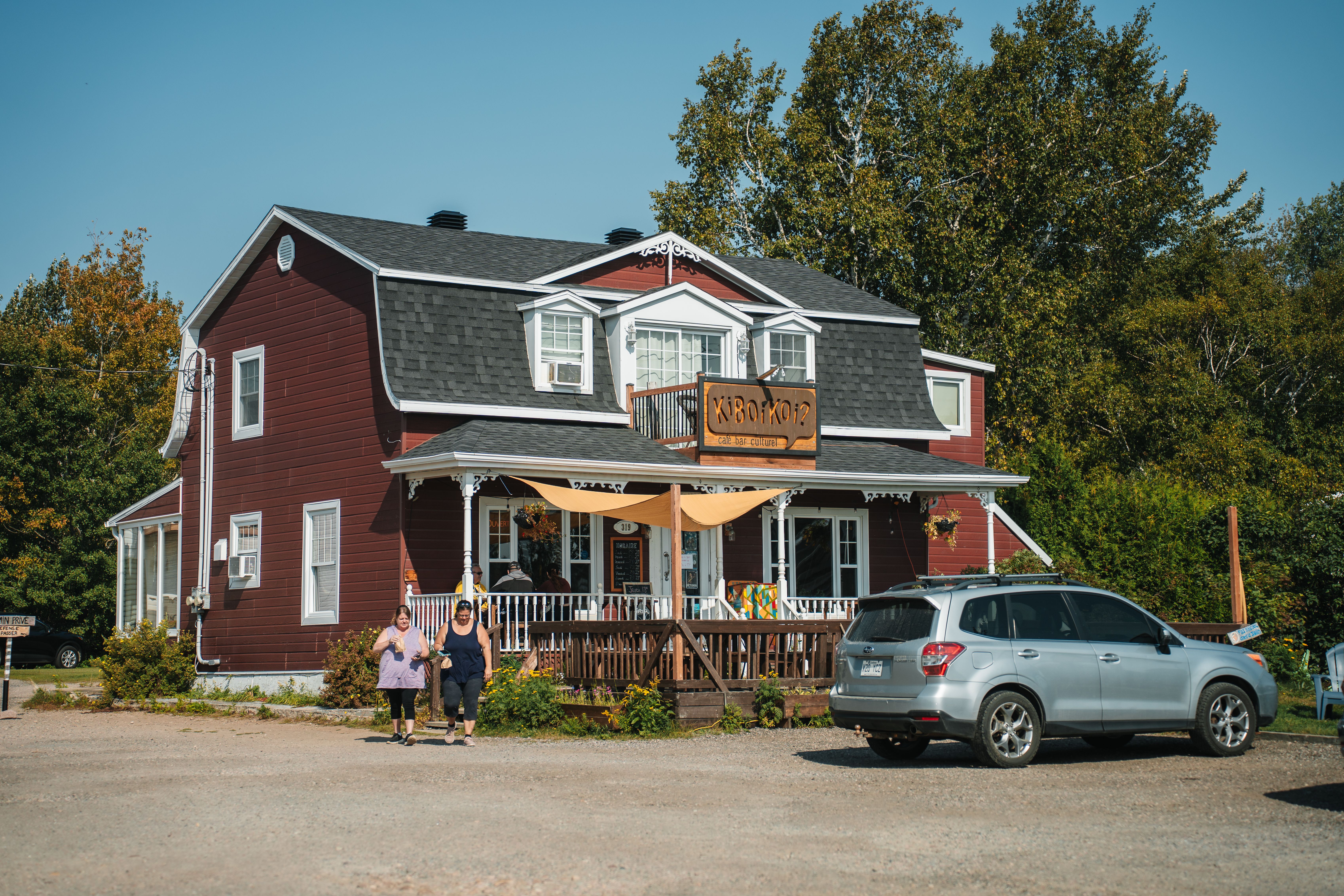 A picturesque red house in Tadoussac, Québec with a charming porch and lush surroundings.