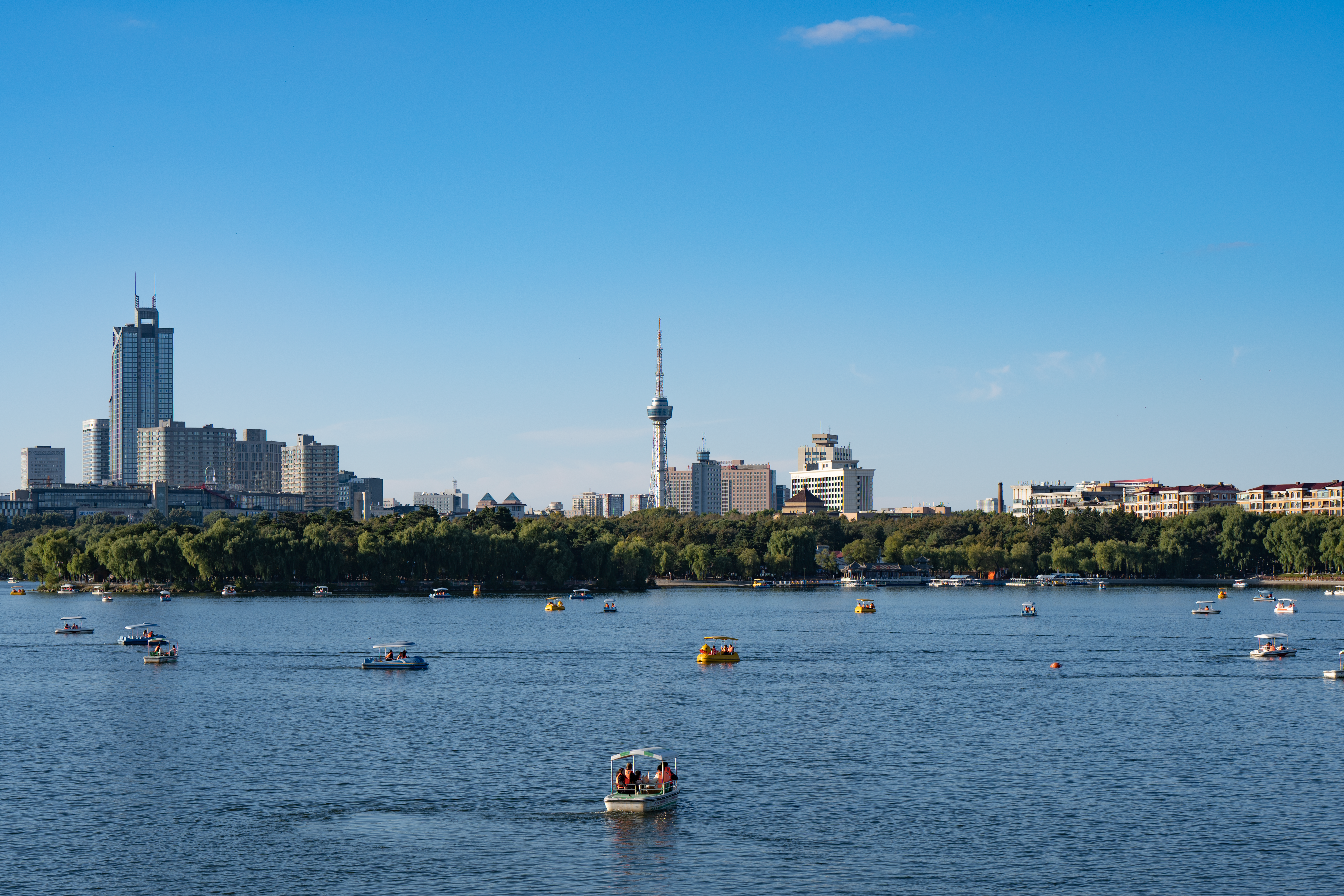 Peaceful afternoon scene of Nanhu Lake with boats and Changchun skyline in view.