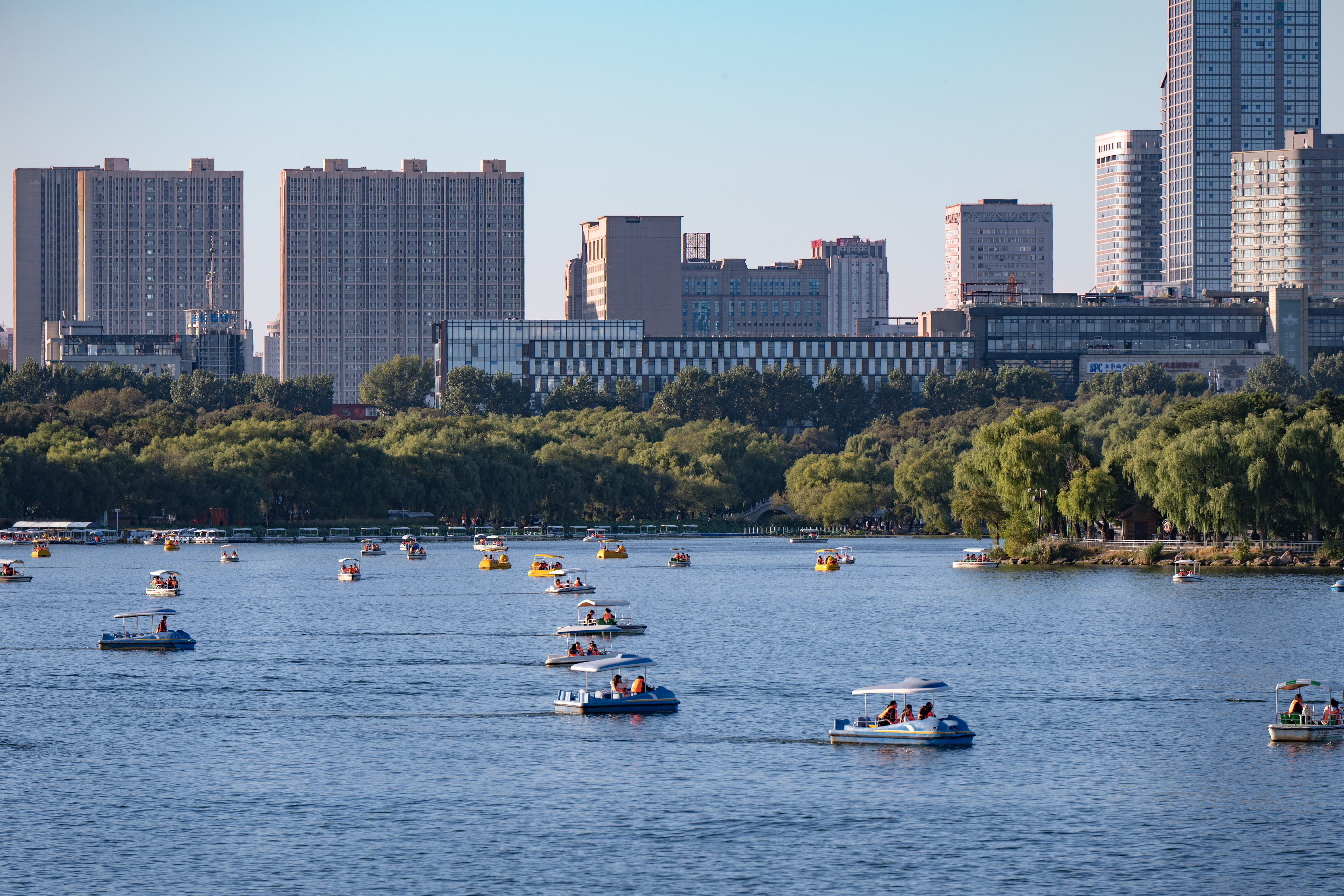 Boats on a serene lake with Changchun's cityscape in the background under a clear blue sky. — lounges at Changchun Airport