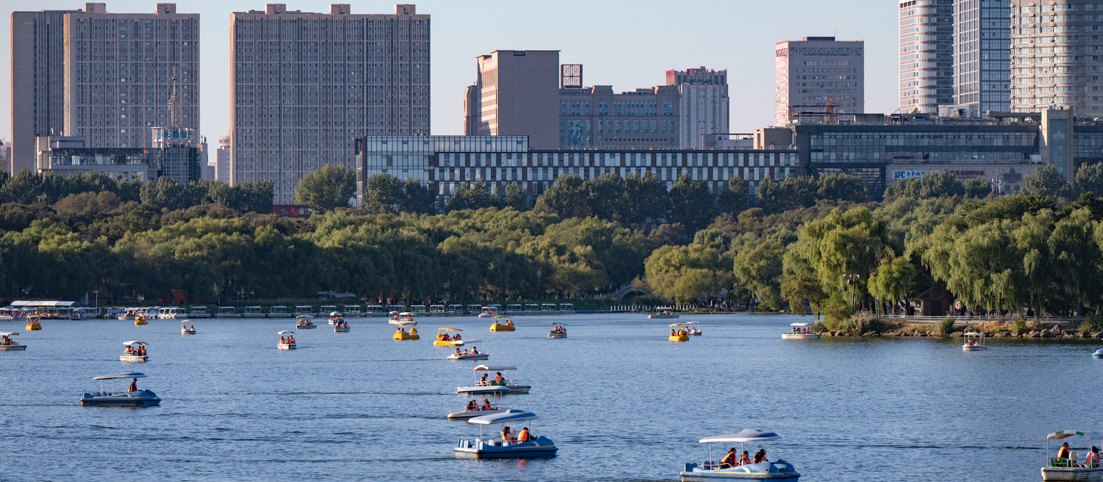 Boats on a serene lake with Changchun's cityscape in the background under a clear blue sky. — flights from Shanghai to Changchun
