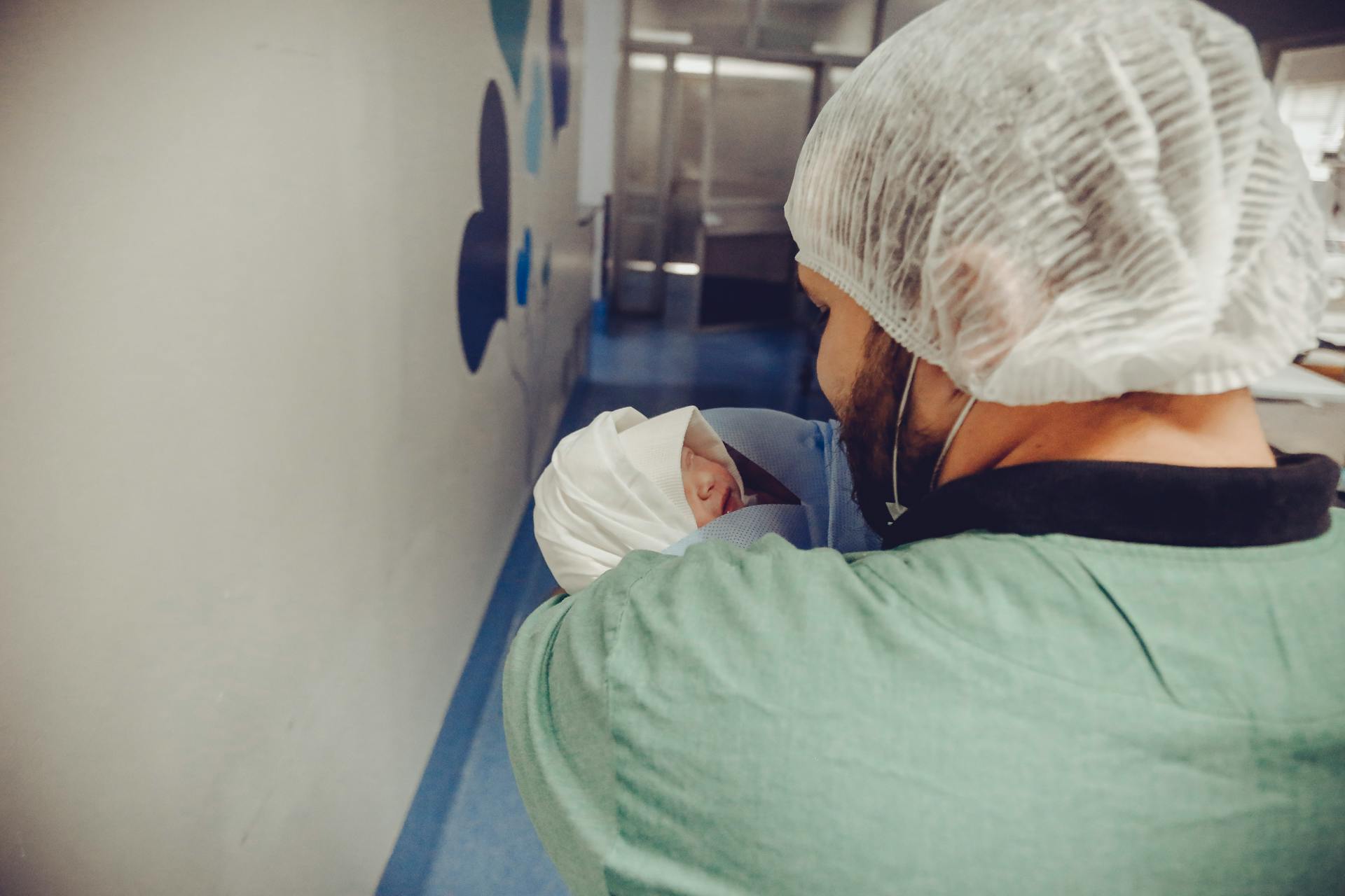 Healthcare worker holding a newborn baby in a hospital hallway, showcasing care and professionalism.