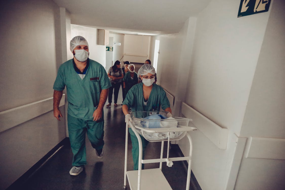 До неузнаваемости акушер и медсестра несут тележку для новорожденного в больнице