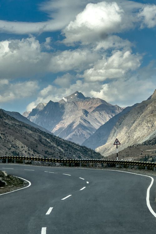Free Breathtaking view of a winding road leading towards majestic mountains under a clear blue sky. Stock Photo