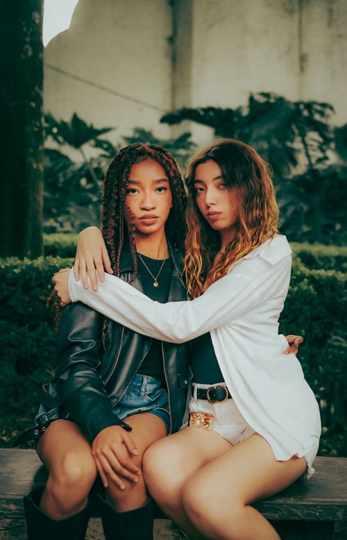 Free Two fashionable young women sitting closely in an outdoor garden setting. Stock Photo