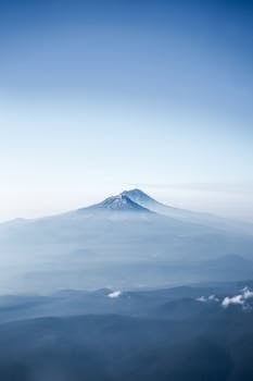 A breathtaking aerial shot of a snow-capped mountain peak surrounded by fog and clouds, capturing the serene beauty of nature.