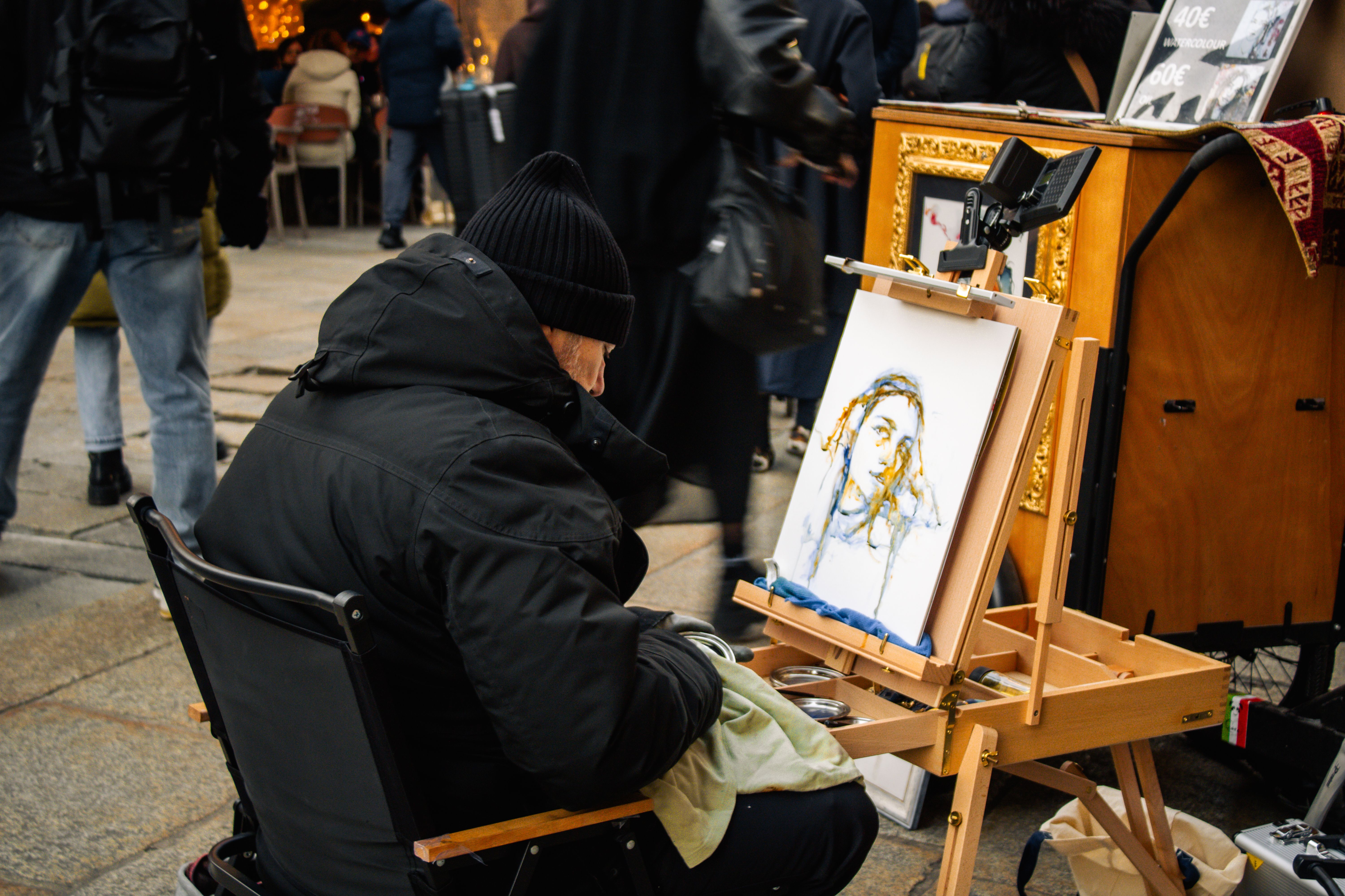 A street artist in Milan captures a portrait amidst a lively outdoor market with people passing by.