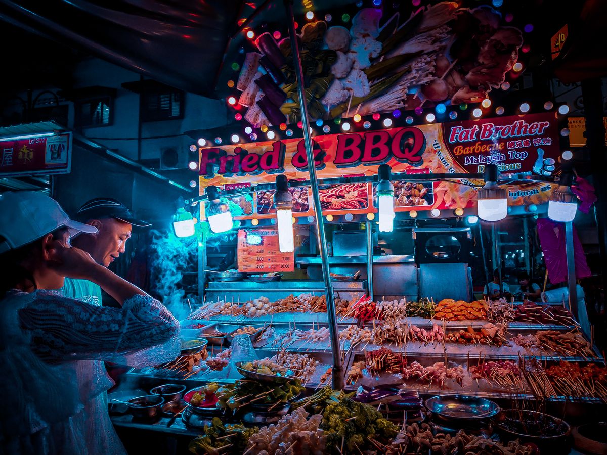 Customer buying food at a brightly lit street stall in a Kuala Lumpur night market
