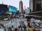 From above of modern metropolis with multistage buildings and asphalt roadway with marking lines and driving automobiles near group of unrecognizable pedestrians crossing road in daylight