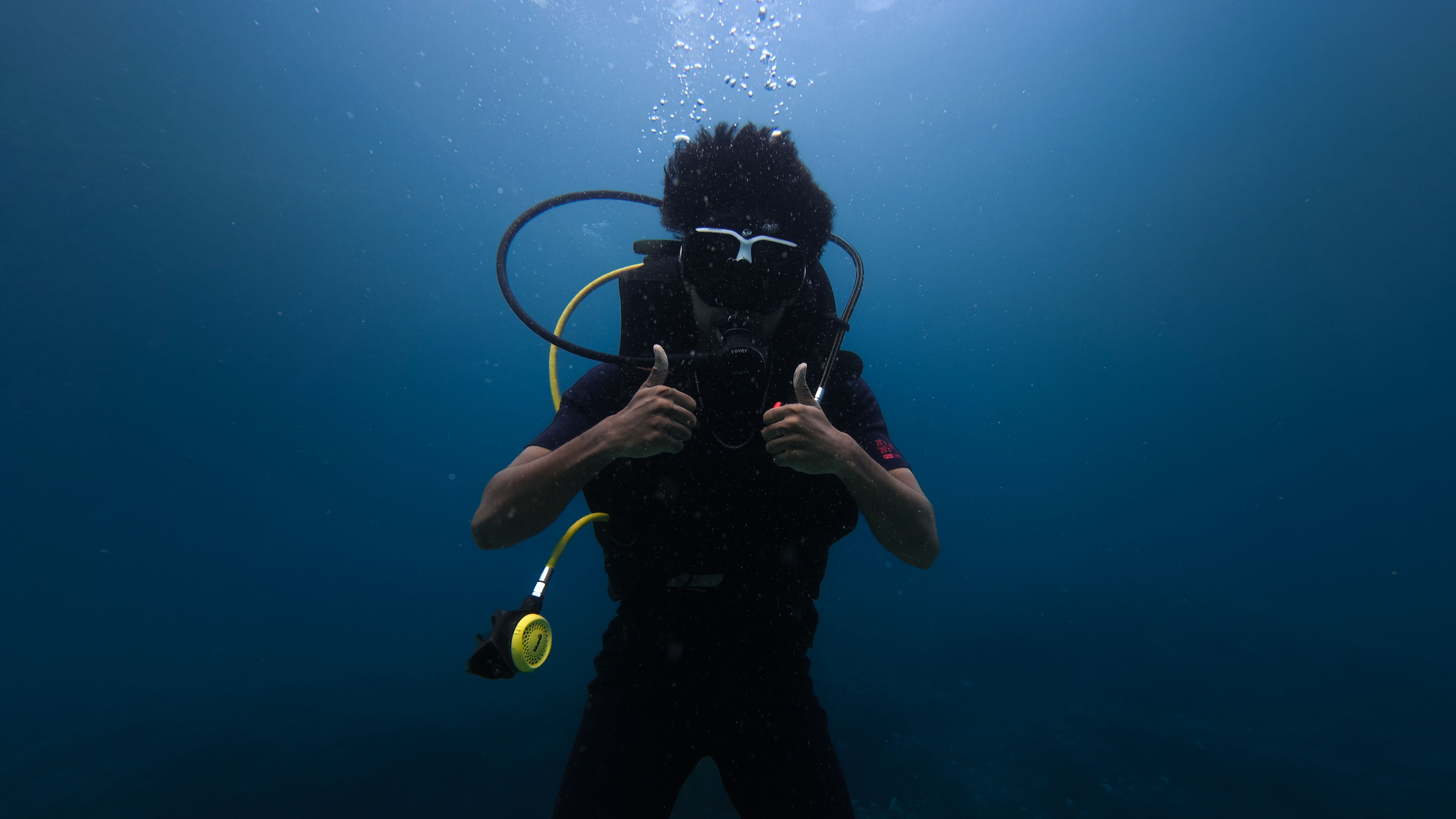 Scuba diver gives thumbs up gesture underwater, showcasing deep sea adventure.