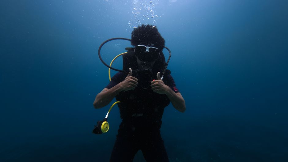 Scuba diver gives thumbs up gesture underwater, showcasing deep sea adventure.