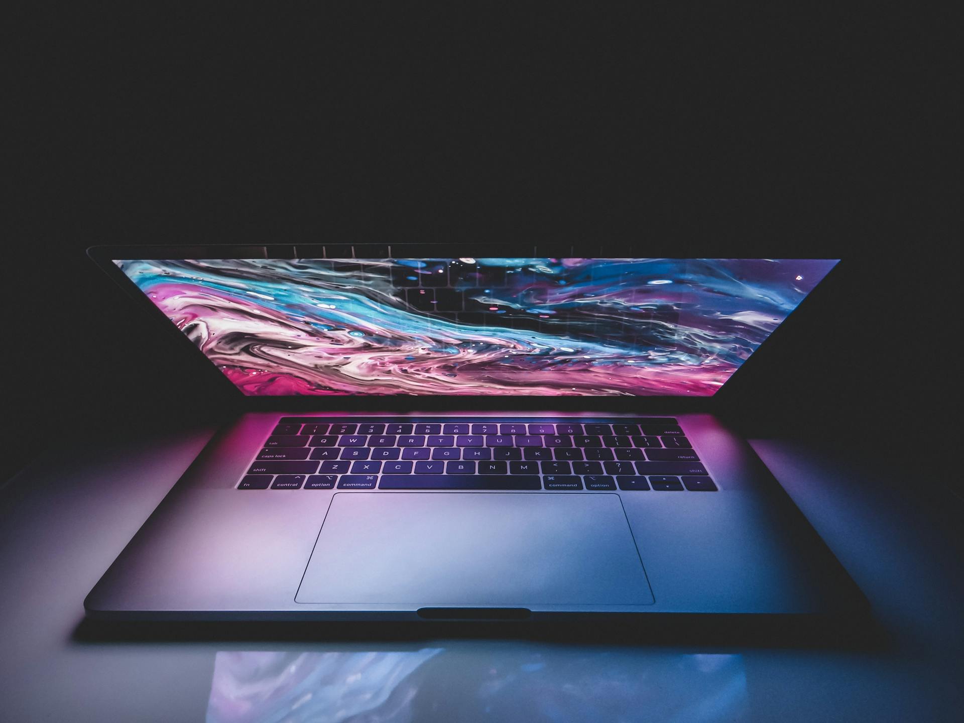 High angle of half opened modern laptop with colorful abstract picture on desktop placed on table in dark room