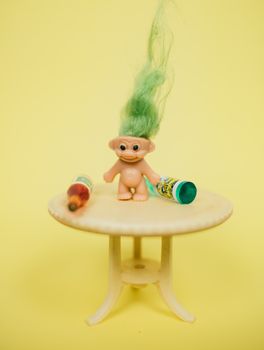 微型桌子上放着一个绿色头发的有趣巨魔玩具，黄色背景前摆着各种瓶子