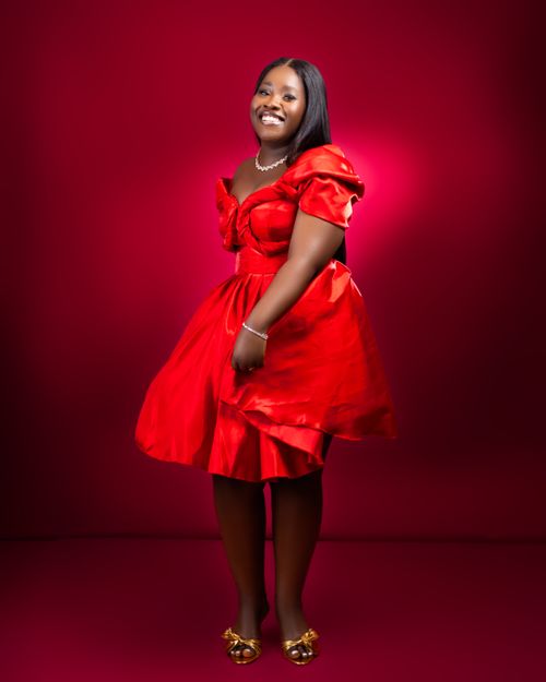 Free A smiling woman in an elegant red dress poses against a matching background in studio. Stock Photo