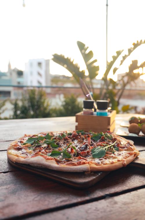 Free Gourmet pizza topped with greens on a rooftop terrace table, captured at sunset. Stock Photo