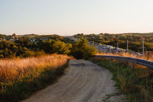 Free Picturesque view of a countryside road leading to a busy highway at sunset. Stock Photo