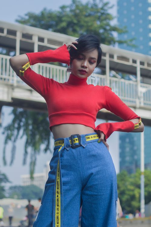 Free Stylish young woman in red top and blue jeans posing in a modern cityscape. Stock Photo