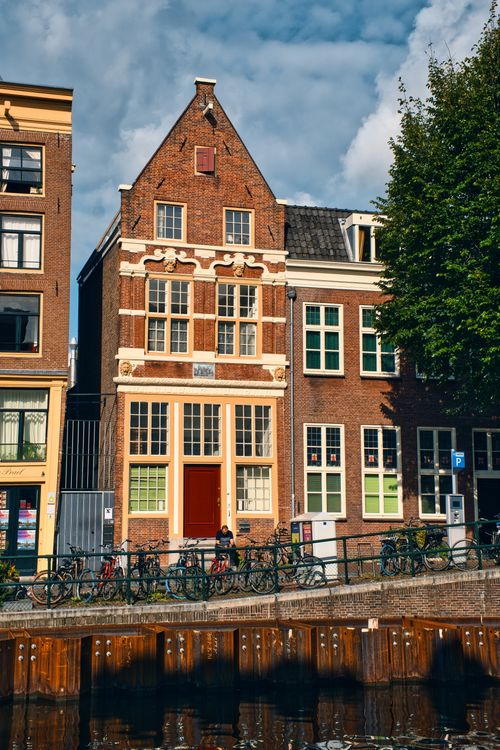 Free Picturesque Amsterdam row houses along a canal with bicycles and clear blue sky. Stock Photo