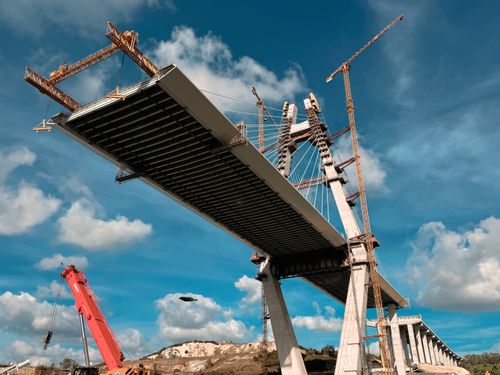 Free A dynamic view of bridge construction with cranes under a blue sky. Stock Photo