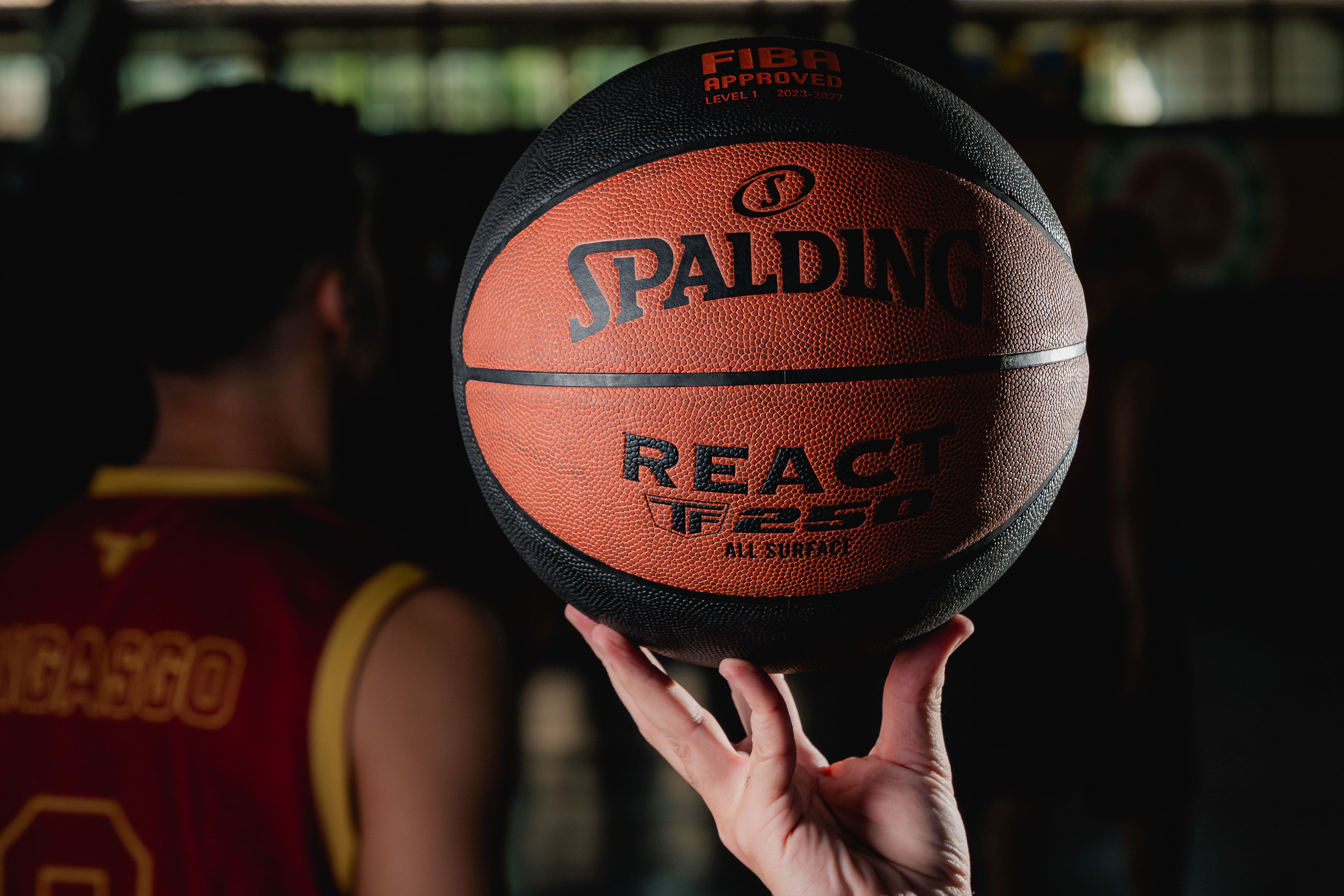 Close-up of a Spalding basketball held by a player in a dimly lit gym setting.