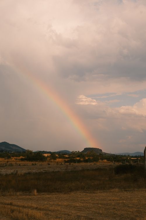 Free A beautiful landscape featuring a vibrant rainbow over a mountain under a cloudy sky. Stock Photo