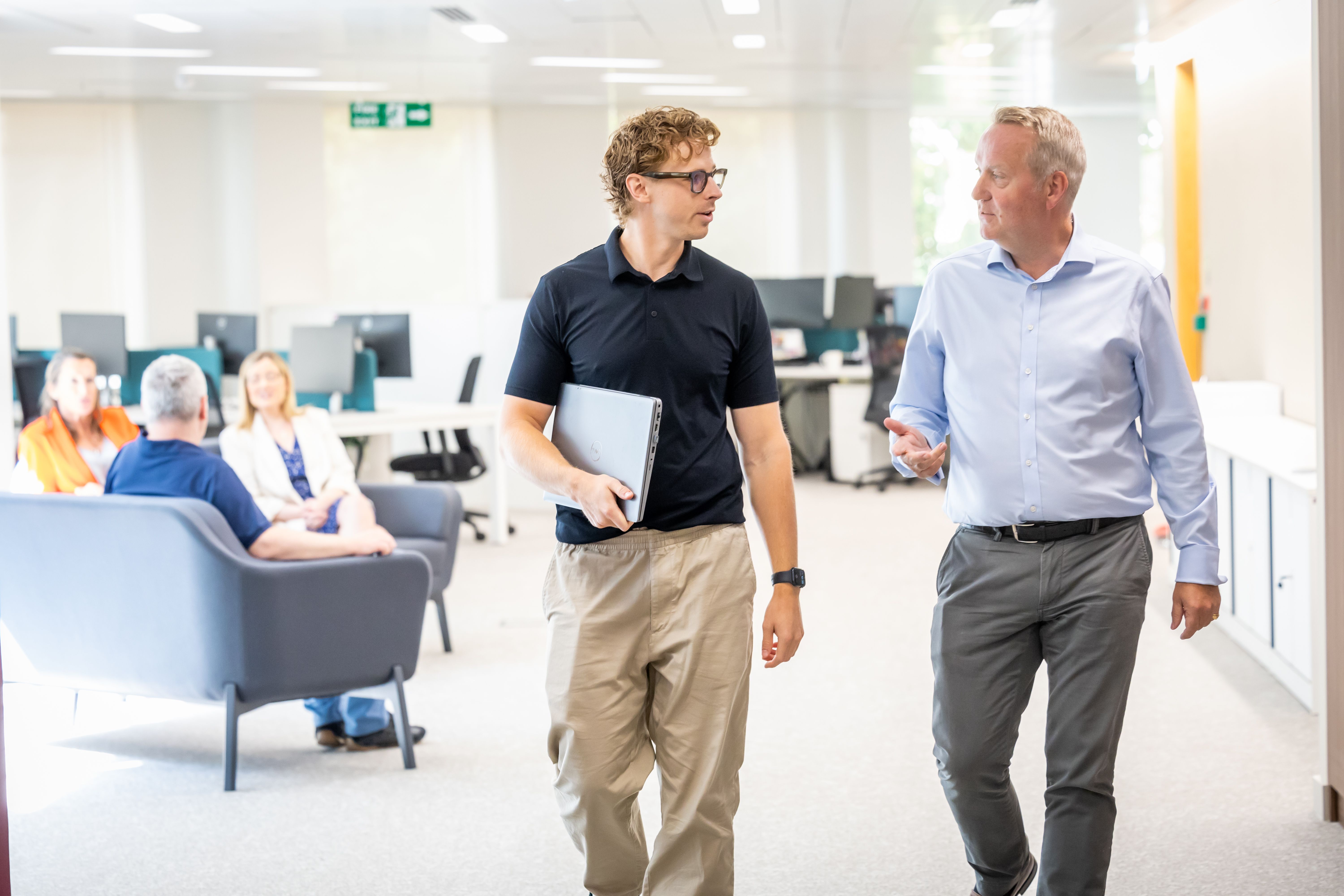 Two colleagues engaged in conversation while walking in a modern office setting, fostering collaboration.
