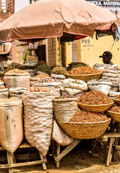 Free A bustling outdoor market scene in Africa featuring sacks and baskets filled with diverse spices and herbs under an umbrella. Stock Photo