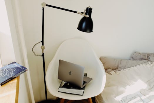 A minimalist bedroom setup with a laptop on a chair and a black reading lamp, ideal for a cozy home office.