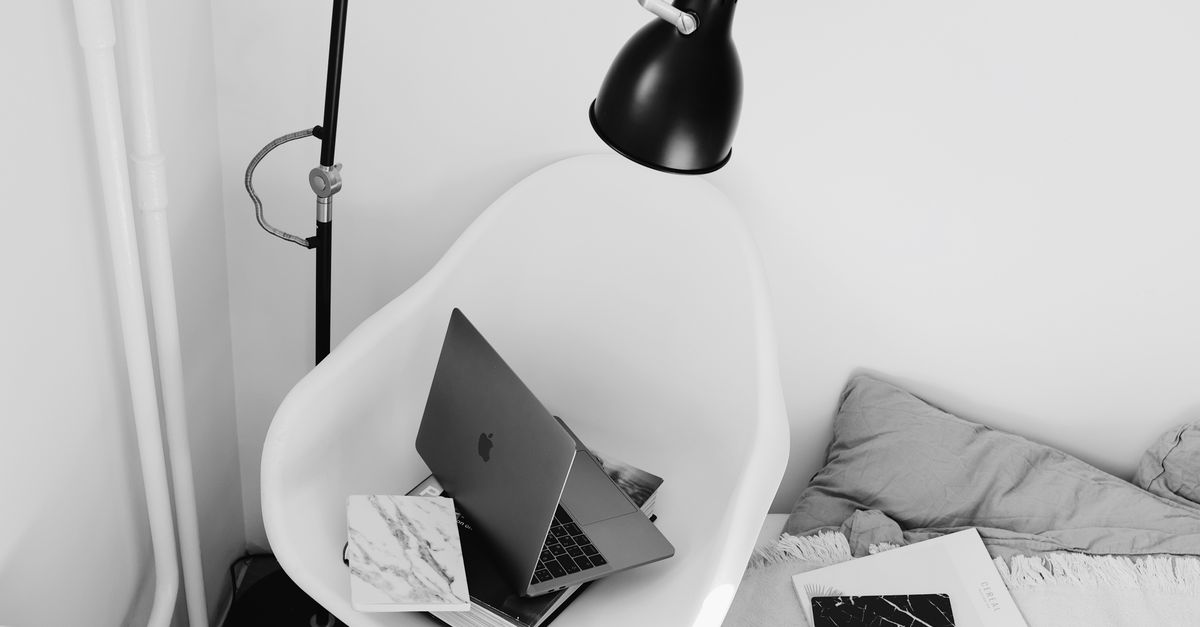 Modern workplace with laptop placed on big book on wooden armchair near wall under lamp in light bedroom