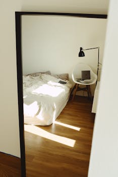 Luminous bedroom with bed, chair, lamp and laptop on wooden flooring.