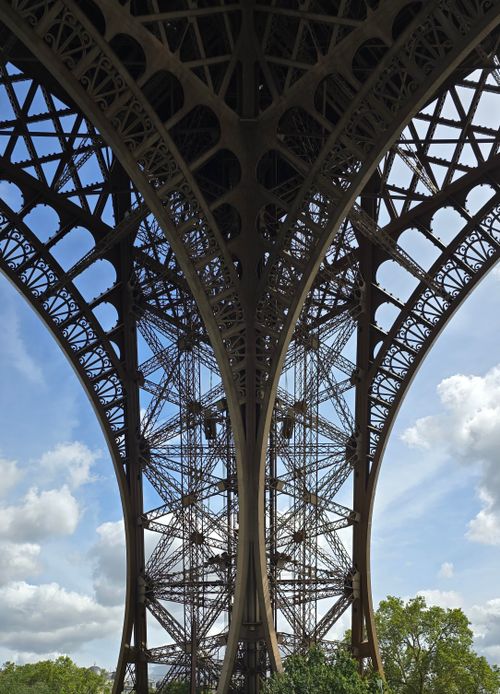 Free Dramatic view of the Eiffel Tower's iron lattice arches set against a blue sky with clouds. Stock Photo