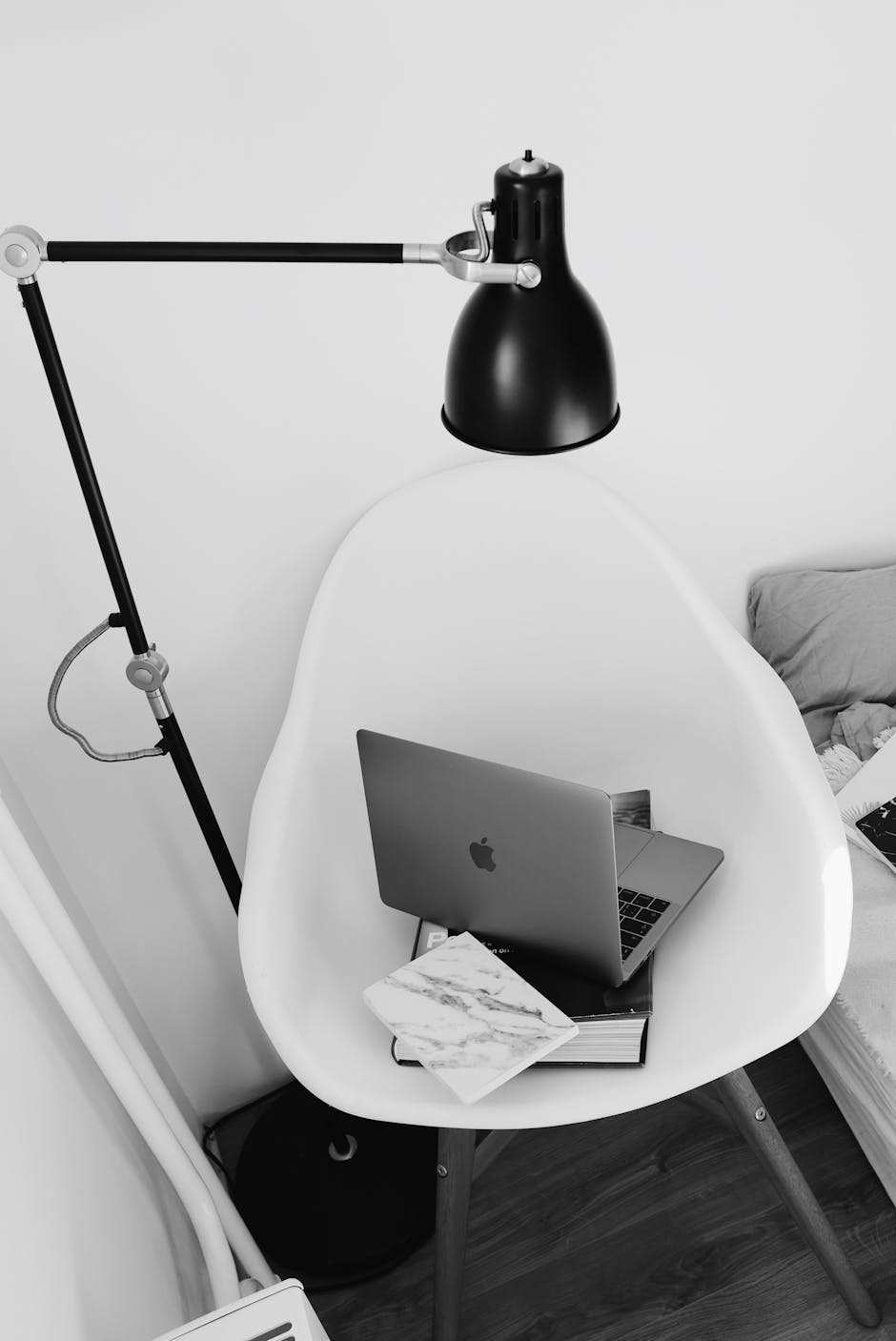 A minimalist black and white workspace featuring a laptop on a chair, under a lamp.